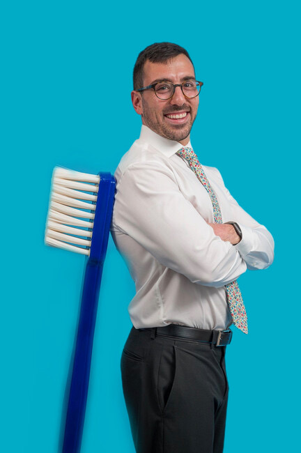 Dr. Scott smiles for a picture leading against a huge toothbrush